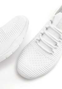 Witte sportieve schoenen met een geperforeerde mesh bovenkant, elastische veters en een stevige, duurzame zool met ribbelaccenten.