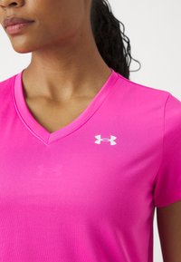 Roza sportska majica s V-izrezom. Izrađena od glatke tkanine, s bijelim logom Under Armour na lijevoj strani prsnog koša.
