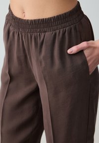 Bruine elastische taillebandbroek met een gladde textuur en zijzakken. De stof valt soepel, met een relaxte pasvorm en een recht ontwerp.