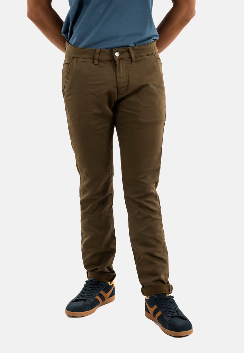 Chinos de algodón marrón con corte slim, que cuentan con bolsillos frontales, cierre de botón y puños remangados, combinados con zapatillas azul marino.