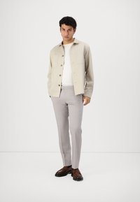 Light beige button-up shirt over a white t-shirt, paired with light gray pants and brown shoes. Minimalist design, tailored fit.