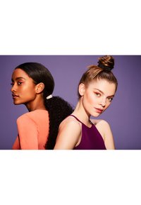 To kvinner med forskjellige frisyrer: den ene har krøllete hår i hestehale og en lys oransje topp, mens den andre har en knute og har på seg en lilla ermeløs topp.