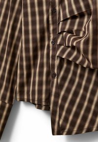 Chemise marron à manches longues avec des rayures verticales beige, boutonnée sur le devant et un poignet plié visible sur le côté droit.