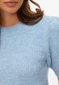 Pull tricoté bleu clair avec un motif texturé, manches courtes et encolure ronde. Le fil présente un effet chiné subtil.