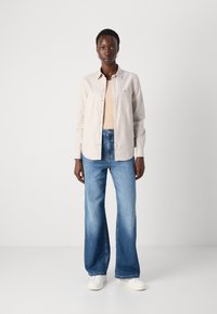 Light beige button-up shirt with a relaxed fit, paired with high-waisted blue denim wide-leg jeans and white sneakers.