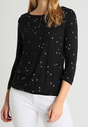 Schwarzes Langarmshirt mit weißem Sternenmuster, rundem Ausschnitt und einem kleinen Schlüssel-Ausschnitt. Weicher Stoff hängt locker.