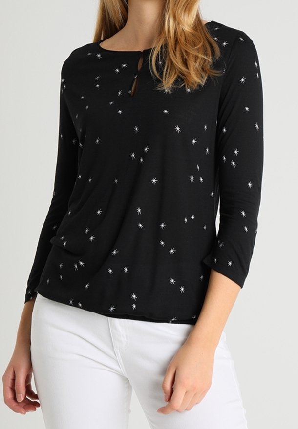 Zwarte langemouwen shirt met een wit sterrenpatroon, ronde halslijn en een kleine sleutelgatdetail. Zachte stof valt losjes.