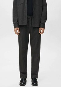 Pantaloni sport gri închis din material moale, cu talie elastică, buzunare laterale și croială lejeră, asortați cu pantofi negri, lustruți.