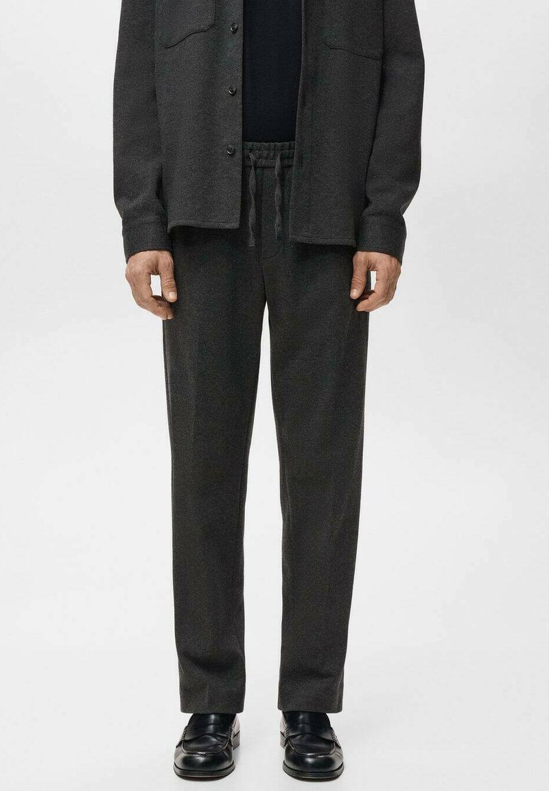 Pantaloni sport gri închis din material moale, cu talie elastică, buzunare laterale și croială lejeră, asortați cu pantofi negri, lustruți.