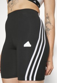 Μαύρες αθλητικές βερμούδες με λευκή τριπλή ρίγα στο πλάι και ανάγλυφο λευκό λογότυπο. Κατασκευασμένες από ελαστικό, υφασμάτινο υλικό που απομακρύνει την υγρασία.