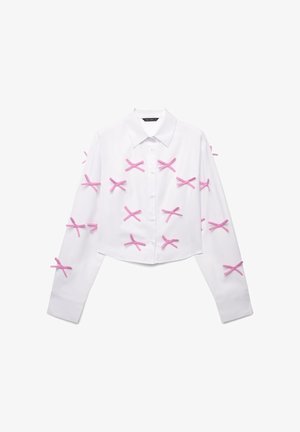 White cropped shirt with long sleeves, featuring multiple pink ribbon accents in a crisscross pattern along the front and sleeves.
