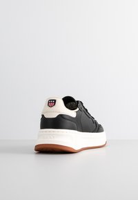 Schwarze Ledersneaker mit beigen Akzenten, runder Spitze und weißer Gummisohle. Verfügt über ein Logopatch mit roten und blauen Details an der Ferse.