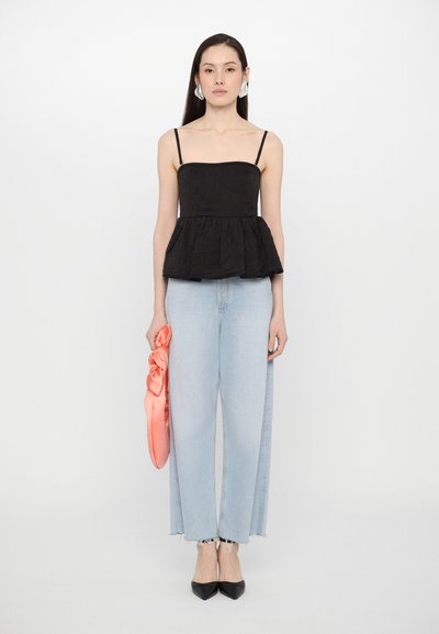 Black peplum top with thin straps, paired with light blue wide-leg jeans. Model holds a shiny coral scarf. Elegant black pointed-toe heels.