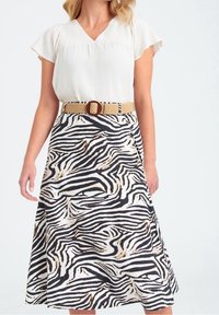 Kvinna som bär en kortärmad vit blus instoppad i en midi-skjort med zebramönster, kompletterad med ett beige flätat bälte och rund spänne.