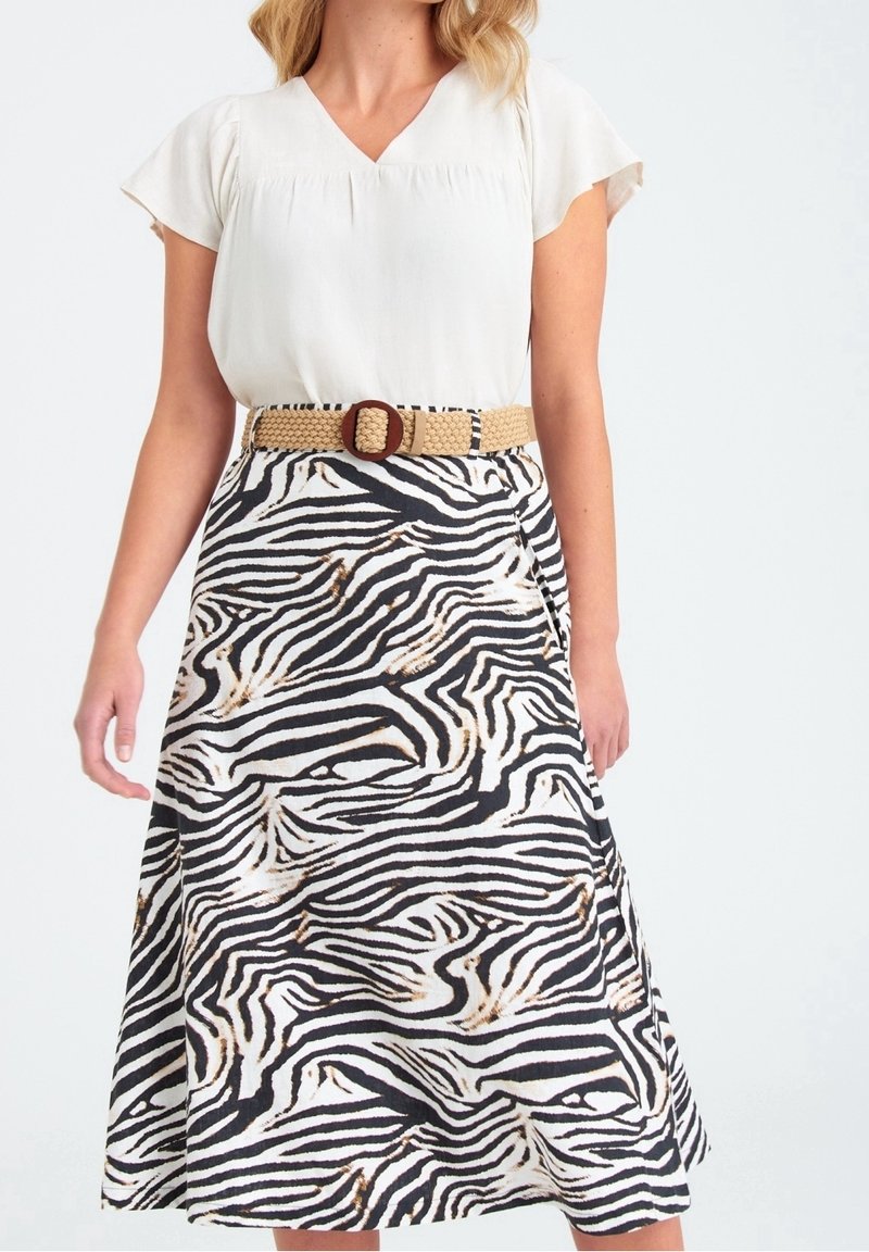 Kvinna som bär en kortärmad vit blus instoppad i en midi-skjort med zebramönster, kompletterad med ett beige flätat bälte och rund spänne.