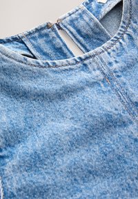 Mėlynos spalvos džinsinis audinys su tekstūruotu raštu. Kaklo iškirptė turi mažą pjūvio dizainą. Siuvimas kontrastingos oranžinės spalvos siūlu.