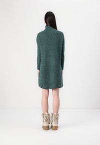 Teal knit dress with a high collar and long sleeves, paired with cream fur-lined boots featuring laces and beige soles.