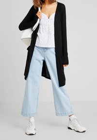 Black long cardigan over a white polka dot top, paired with light blue wide-leg jeans and white sneakers. Simple design with pockets.