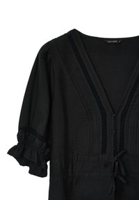 Blusa nera con maniche corte a volant, scollo a V, tessuto strutturato e cuciture decorative lungo il collo. Si annoda in vita.