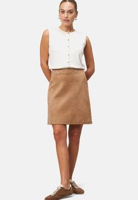 Haut sans manches blanc avec des boutons, associé à une jupe en daim beige ornée de clous argentés le long de l'ourlet. Des baskets marron complètent le look.