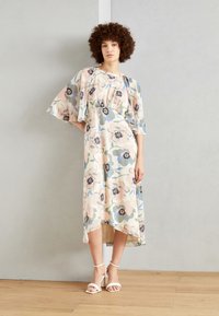 Floral mid-length dress with flutter sleeves, featuring pastel colors and dark floral patterns. Accompanied by strappy white heels.