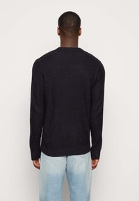 Navy knitted sweater with a textured pattern, crew neckline, and long sleeves, paired with light blue denim jeans.