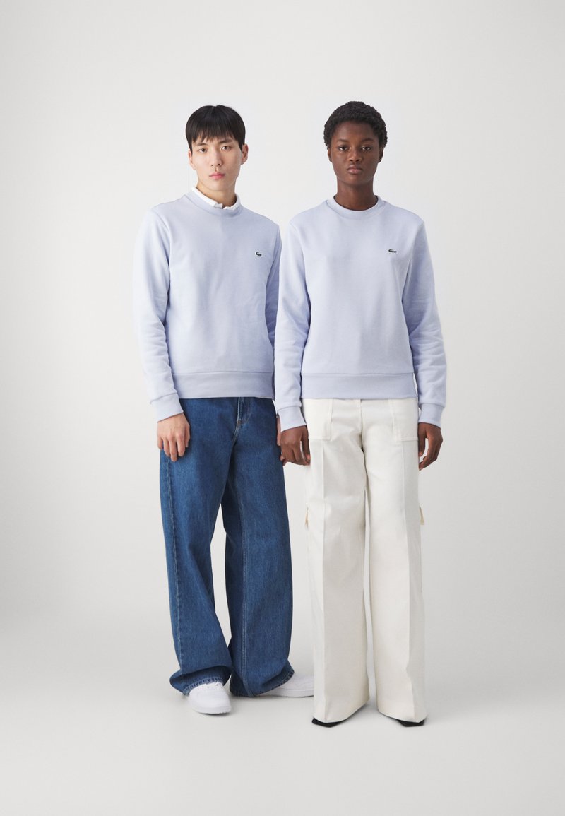 Lichtblauwe crewneck sweatshirts met geribde boorden, gedragen met losse spijkerbroeken en witte broeken. Bevat kleine logo-accenten op elk sweatshirt.