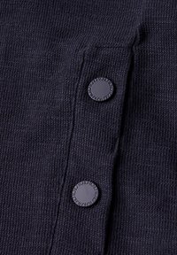 Námořnická tkanina s texturovaným vzorem obsahuje dvacet zaoblených černých knoflíků na léze. Knoflíky mají vyražené písmo kolem svých okrajů.