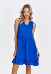 Niebieska sukienka bez rękawów z dekoltem w kształcie litery V, marszczoną talią i falbaną u dołu. Wykonana z lekkiego materiału o gładkiej strukturze.