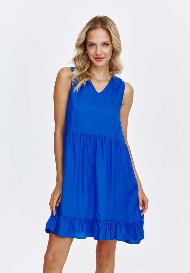 Niebieska sukienka bez rękawów z dekoltem w kształcie litery V, marszczoną talią i falbaną u dołu. Wykonana z lekkiego materiału o gładkiej strukturze.