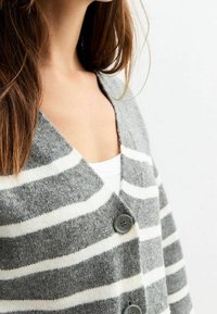 Szary i biało paskowany kardigan wykonany z miękkiego materiału, z dekoltem w serek, z trzema guzikami i luźnym krojem.