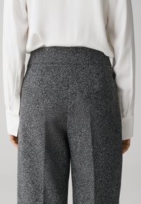 Grijze textuurbroek met een hoge taille, vergezeld van een witte blouse. De stof heeft een geweven patroon en een gladde afwerking.