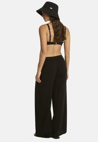 Mujer que lleva un sombrero tipo bucket negro, un top de sujetador negro con tirantes ajustables y pantalones de pierna ancha y talle alto negros, mirando hacia la izquierda.