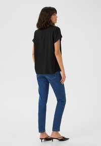 Black short-sleeved top worn with blue jeans. The top has a loose fit and soft texture, while the jeans are form-fitting with a classic cut.