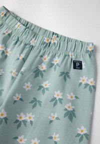 Lichtgroene stof met een bloemmotief met witte bloemen en gele middens. Elastaan tailleband met een klein merklabel.