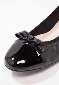 Czarne lakierowane baleriny z kokardką na gładkim czubku i teksturowanymi bokami, charakteryzujące się elastycznym i zaokrąglonym kształtem.