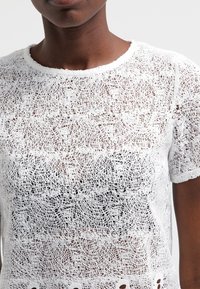 Top bianco all'uncinetto con un design a tessitura aperta e texture, maniche corte e scollatura rotonda. Notevole per il suo motivo intricato.