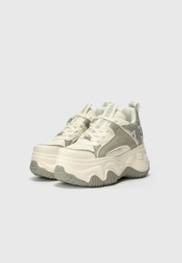 Chunky sneakers med en hvit og lys grå fargekombinasjon, lær- og mesh-materialer, utpreget såle og dekorative stropper.