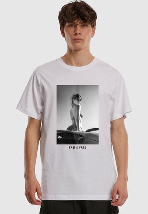 Jeune homme portant un T-shirt blanc avec une photo en noir et blanc d'une femme en bikini près d'une voiture, texte « FAST & FREE » sous la photo.