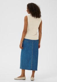 Un haut sans manches beige associé à une longue jupe en denim bleue, avec une coupe droite, deux poches arrière et une couture au centre.