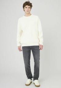 Pull beige clair, texture côtelée, col rond. Jean gris foncé, coupe droite, aspect usé. Baskets blanches avec semelles beiges. Fond neutre.