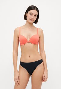 Koraal push-up bh met dunne bandjes, gladde textuur en voorgevormde cups; gecombineerd met een zwarte bikini onderbroek, naadloos design.