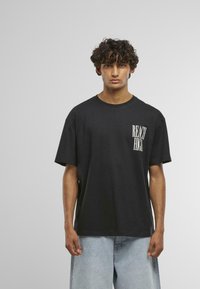 Black cotton t-shirt with short sleeves, featuring "REACH HIGH" graphic in white on the left chest. Paired with light denim shorts.
