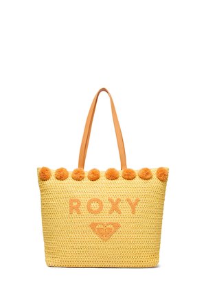 Gelbe gewebte Tragetasche mit orangen Pompons oben, hellbraunen Griffen und dem Wort "ROXY" mit einem Herz-Logo auf der Vorderseite.