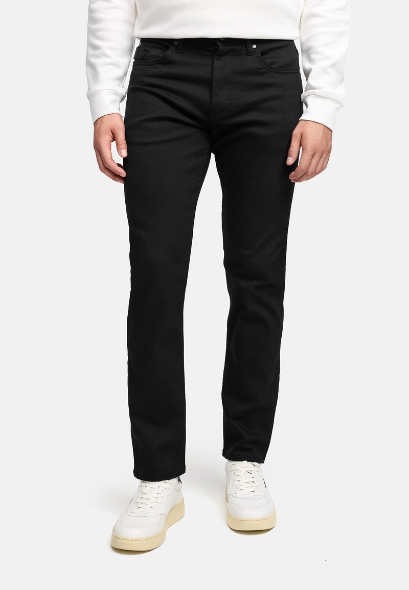 Jeans neri in denim con vestibilità slim, design a cinque tasche e dettagli di cucitura sottili, indossati con sneakers bianche e una felpa leggera.