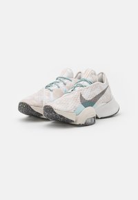 Scarpe atletiche leggere con tomaia testurizzata color crema e accenti blu, caratterizzate da un'importante swoosh nera e suola in gomma maculata.