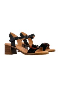 Schwarze Sandalen mit einem glatten Lederoberteil, breitem Riemendesign und moderatem Blockabsatz. Auffälliges Schnallendetail am vorderen Riemen.