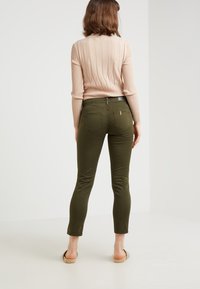 Dunne olijfgroene broek gemaakt van rekbaar materiaal, met achterzakken en een middelhoge taille, gecombineerd met een lichtroze ribgebreide trui.