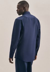 Camicia a maniche lunghe color navy con polsini abbottonati, tessuto morbido e colletto classico. Vestibilità su misura con orlo curvo e design minimalista.
