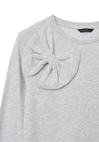 Haut gris clair à manches longues avec encolure ronde, doté d'un grand nœud en tissu sur l'épaule gauche et d'une petite étiquette noire à l'intérieur du col.
